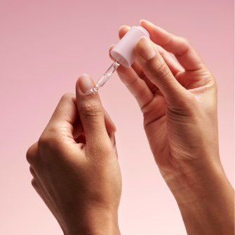A person is holding a dropper with a pink background.