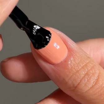 A hand using a brush to apply black nail polish over a peach nail.