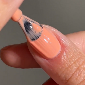 A hand painting a nail with peach-colored nail polish.