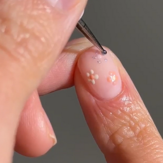 A hand paints a nail with a fine brush, with delicate floral decorations on a pale pink base.