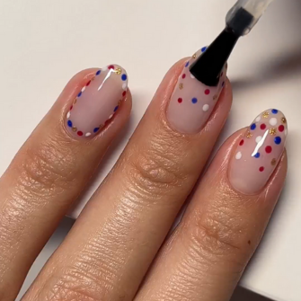Nails with transparent polish and colorful dots, decorated with a top coat.