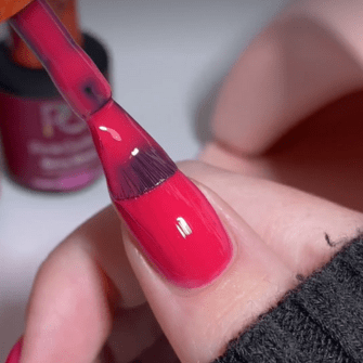 A close-up of a hand painting a nail with bright pink nail polish.