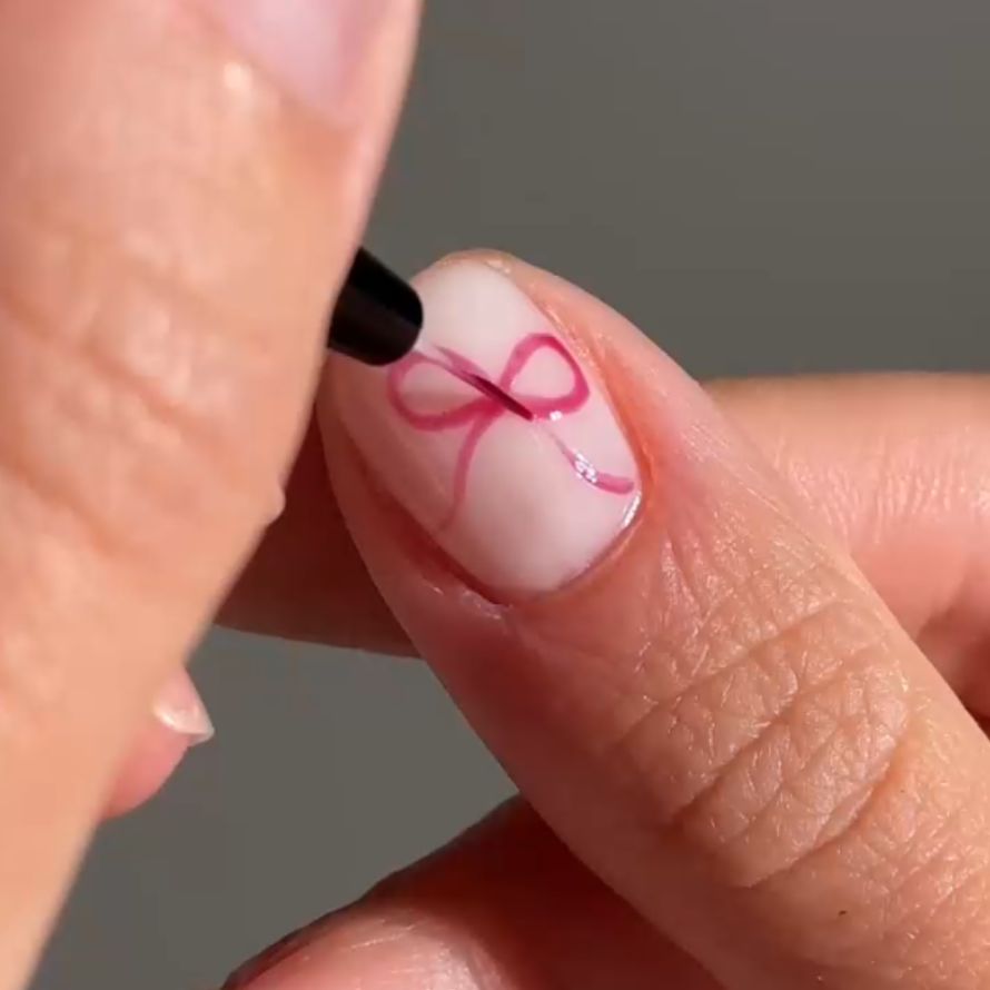 Close-up of a nail on which a pink bow has been painted with a brush.