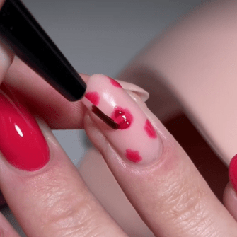 A hand painting another hand with red nail polishes with red dots.