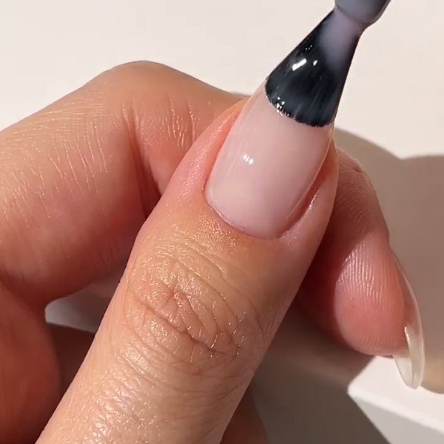 Hand with nail being painted with light pink nail polish with a brush.