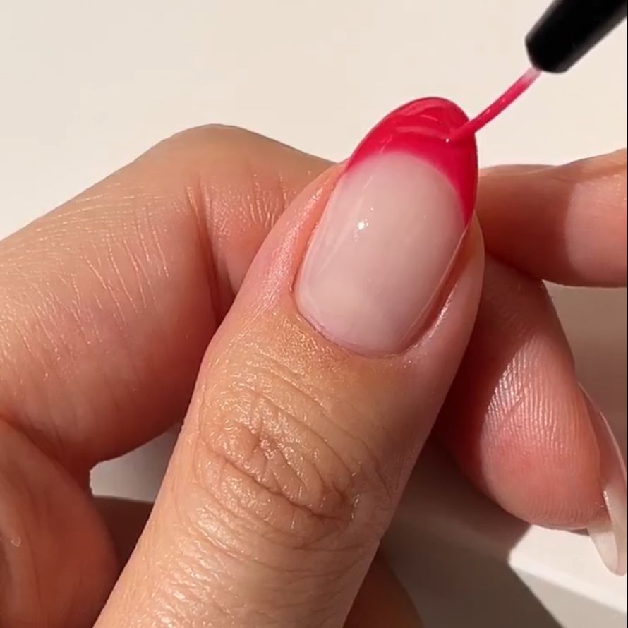 A hand that is busy applying pink nail polish to the tip of a nail.