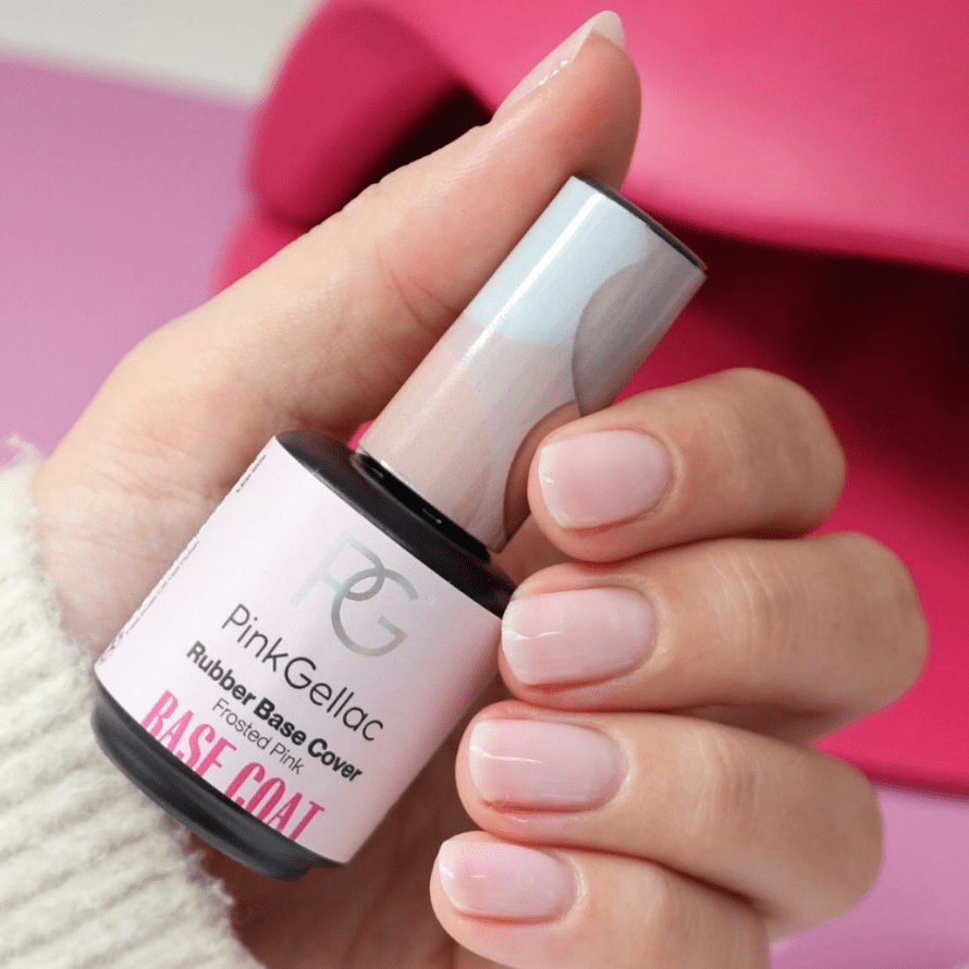 A hand with manicured nails holds a bottle of Pink Gellac Rubber Base Cover in the color Frosted Pink, against a pink background.