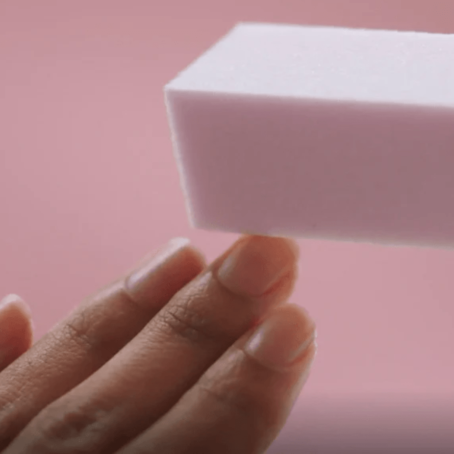 "Close-up of a hand holding a pink foam block against a pink background."