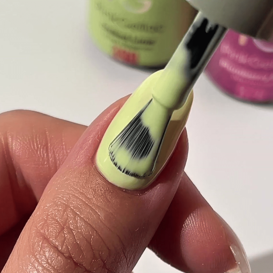 A close-up of a hand using a brush to apply pale yellow nail polish to a nail.