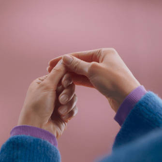 Two hands clasped together in front of a pink background, both with colored sleeves.