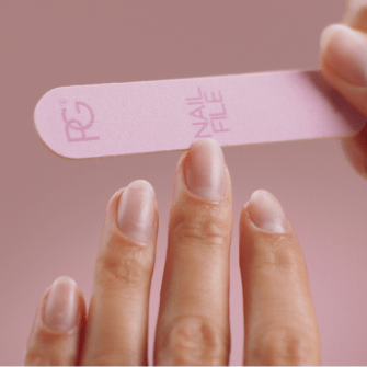 Person filing nail with a pink nail file against a pink background.