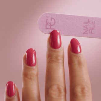 Nails with pink nail polish are filed with a pink nail file against a pink background.