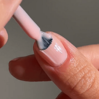 A close-up of a nail being painted with light pink nail polish.