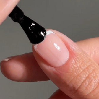 A brush applies black nail polish to a fingernail.