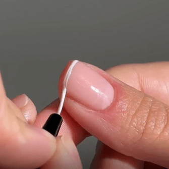 Alt tag: A person uses a small brush to apply a thin white line to a natural nail against a gray background.