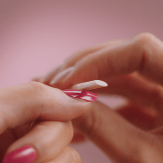 A close-up of a hand with pink painted nails while the other hand carefully files a nail.