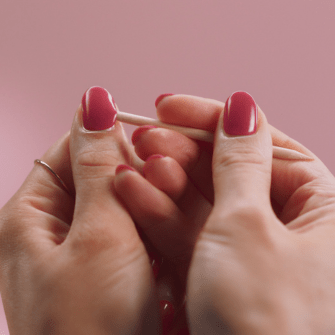 Alt-tag: Hands with pink painted nails use a wooden marker against a pink background.