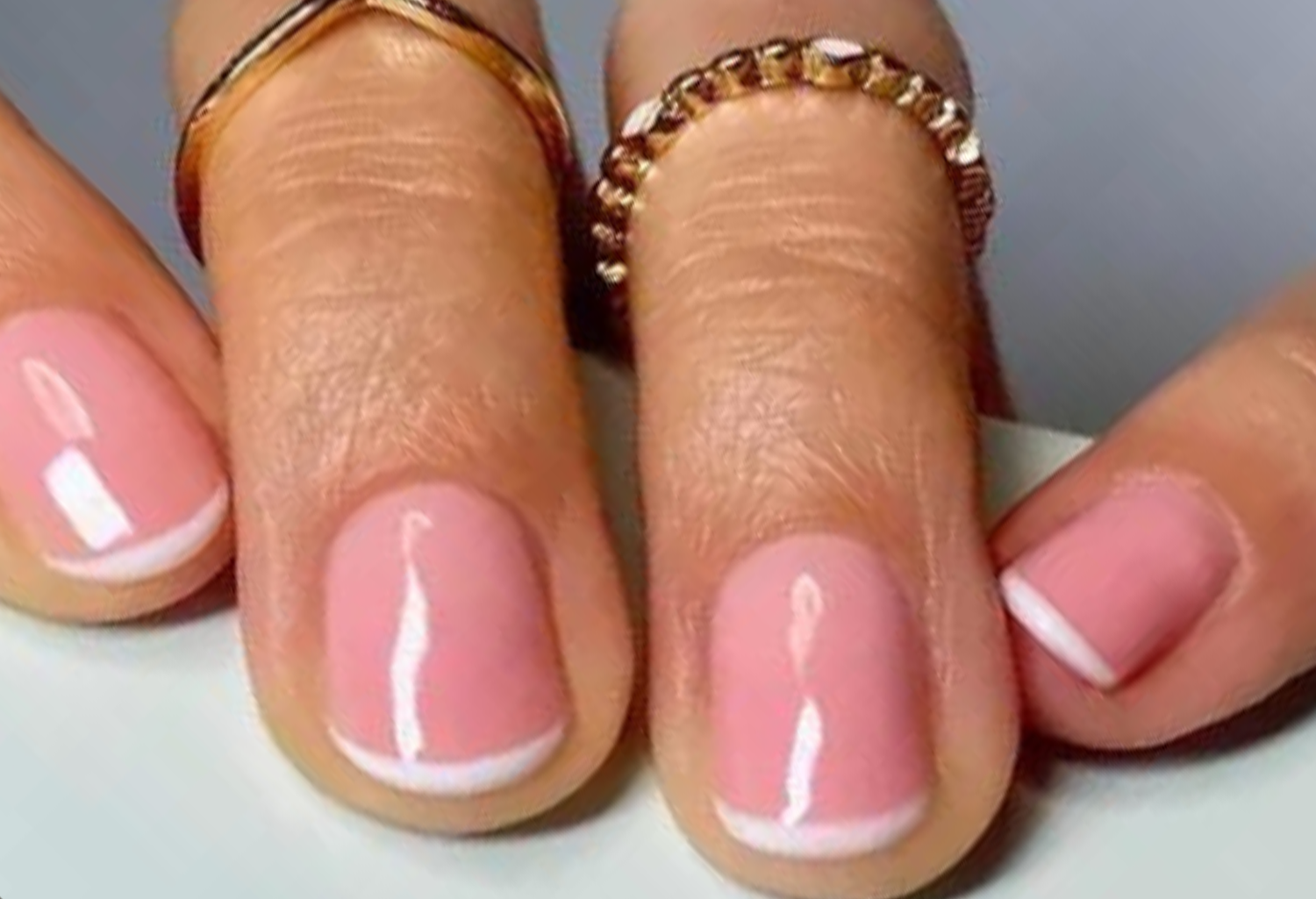 Nails with a French manicure design on three fingers, surrounded by gold rings.