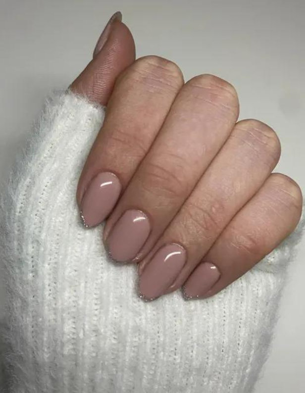 Hand with light pink painted nails against a white knitted sweater.