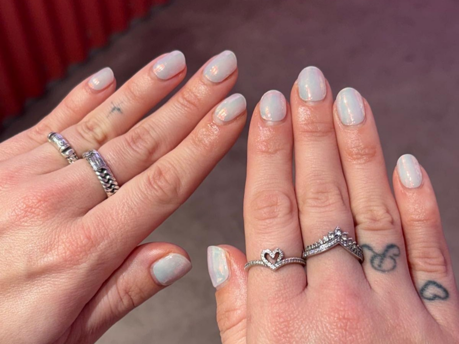 Hands with light pink nails, several silver rings and subtle tattoos.