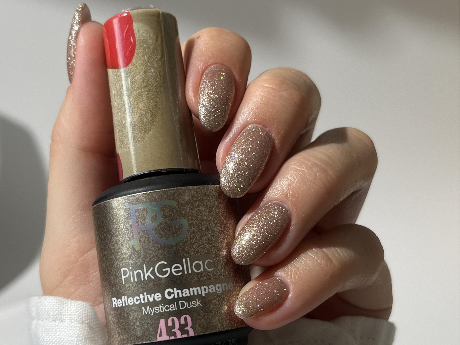 Hand with glittering nail polish and a bottle of Pink Gellac Reflective Champagne Mystical Dusk, number 433.