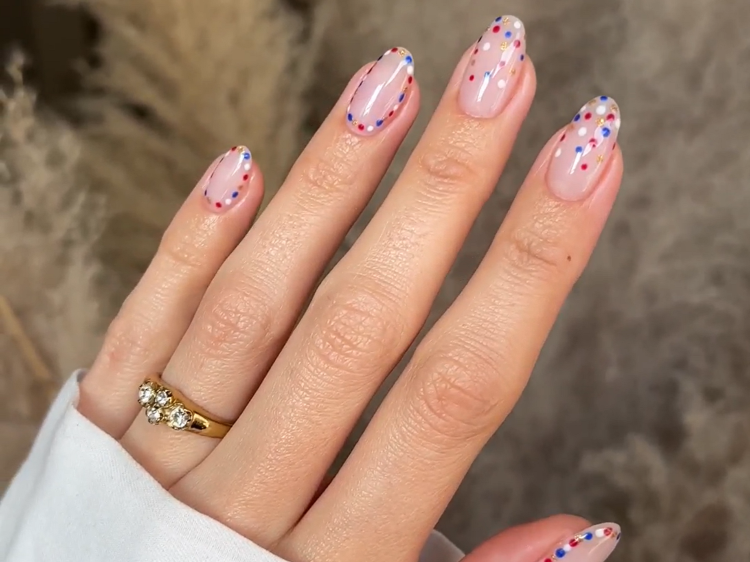 Hand with nails decorated with colorful dots and a gold ring with three diamonds.