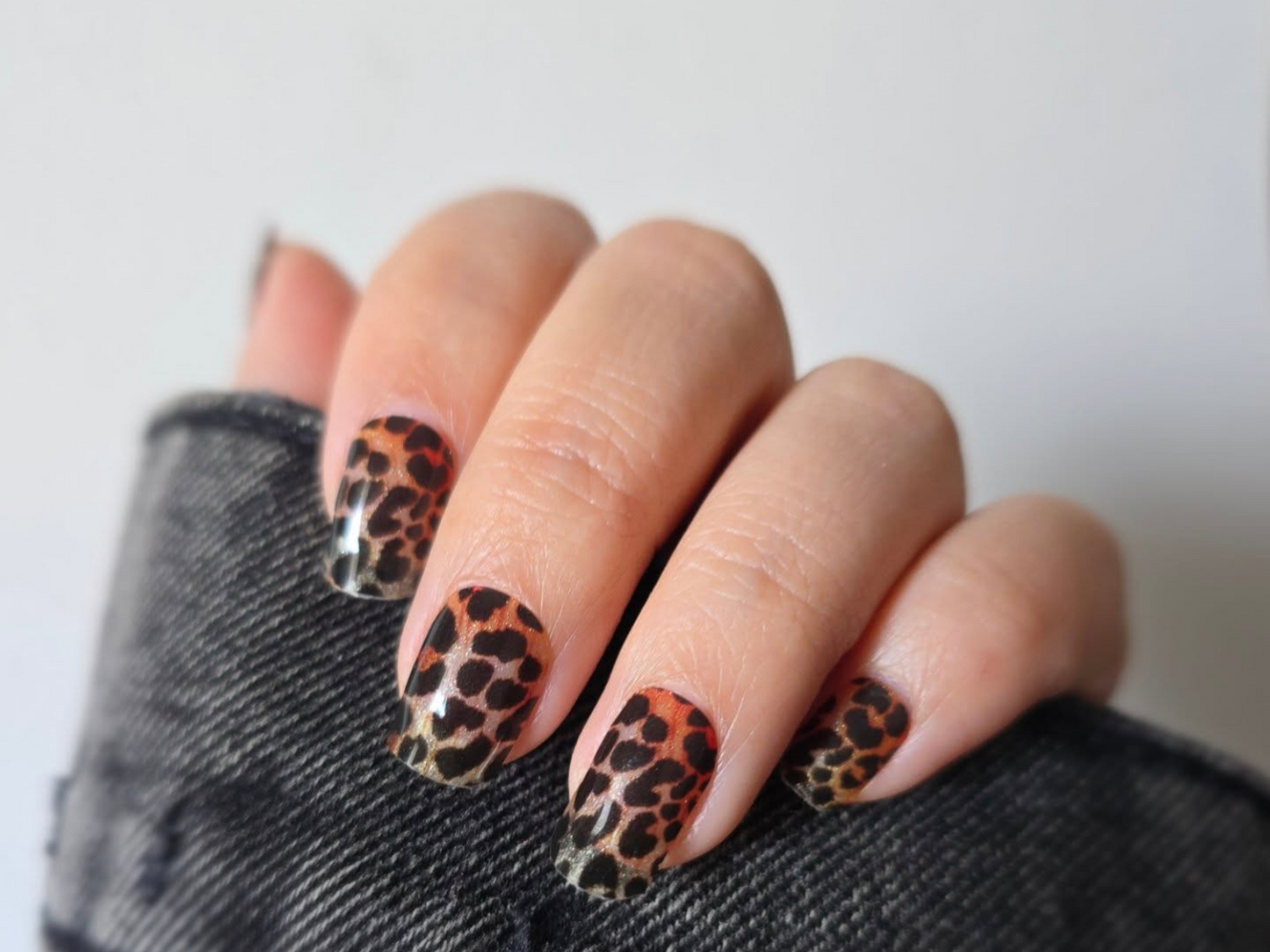 Close-up of a hand with nails in a leopard print, held against a dark fabric.