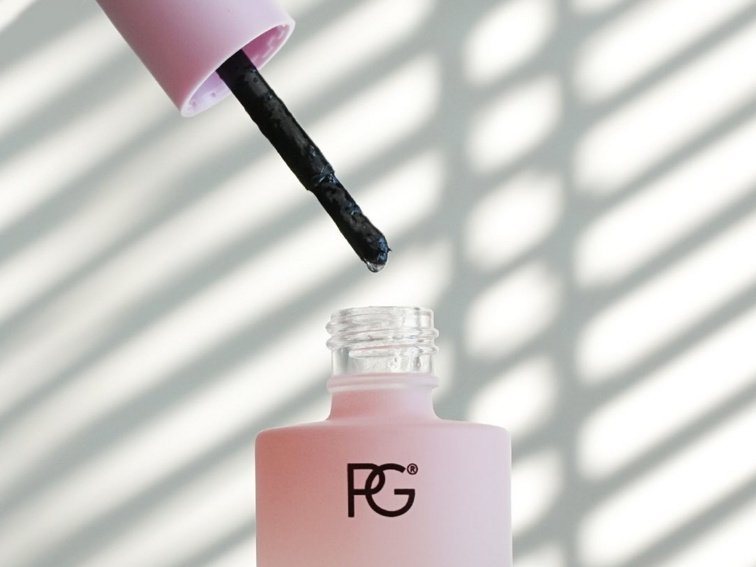 Pink nail polish bottle with the logo "PG" and an opened brush against a striped background.
