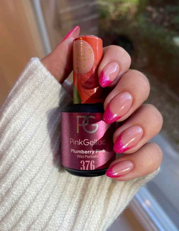 A hand with bright pink nail tips with glitter holds a bottle of Pink Gellac Plumberry Pink nail polish.