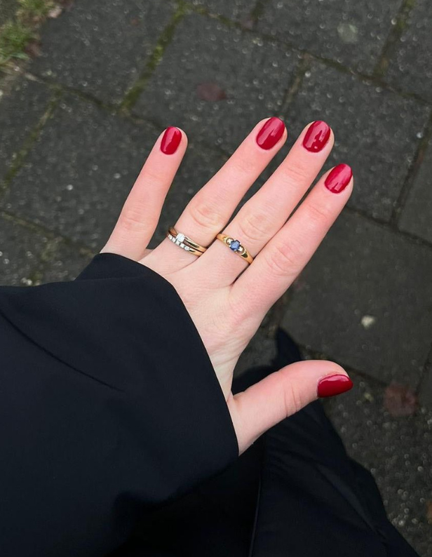 A hand with red nail polish and two rings, one©©of which with a blue stone, against a stone pavement.