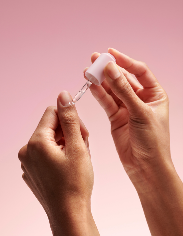Hands holding a pipette with a pink background.