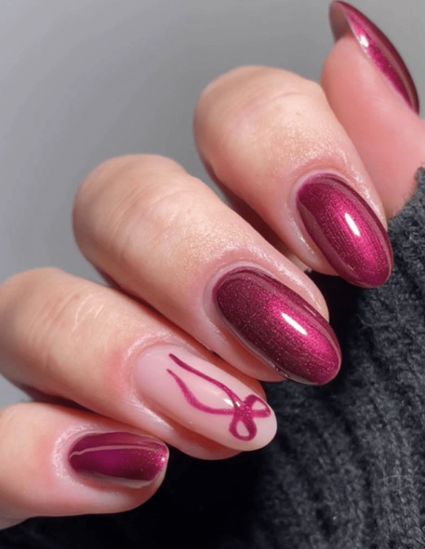 Hand with painted nails in shiny dark red and a decorative pattern on the ring finger.