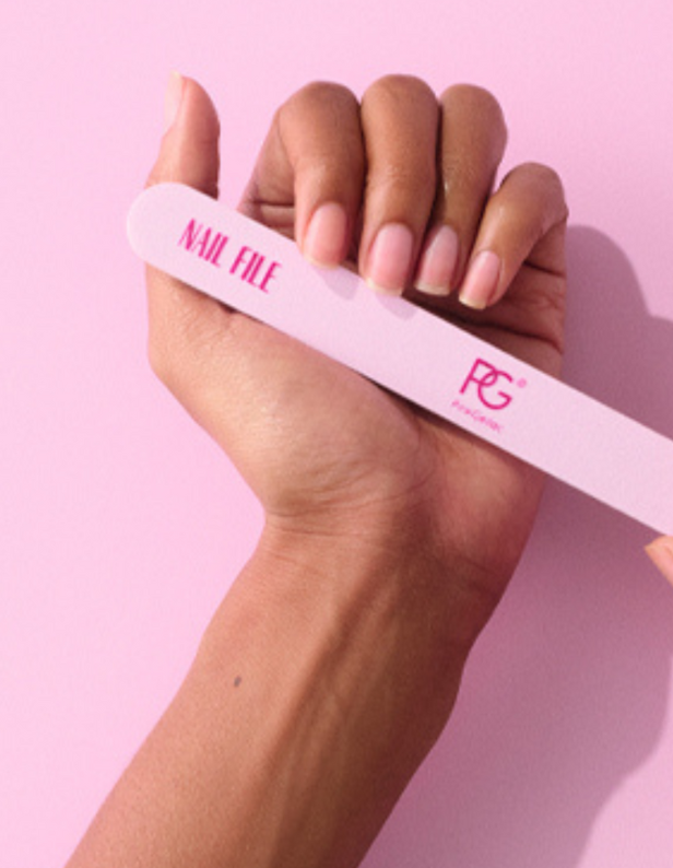 Close-up of a hand with neatly groomed nails holding a pink nail file against a pink background.