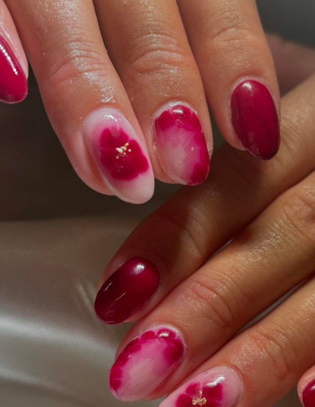 Close-up of hands with dark pink and white nails, some with floral motifs.