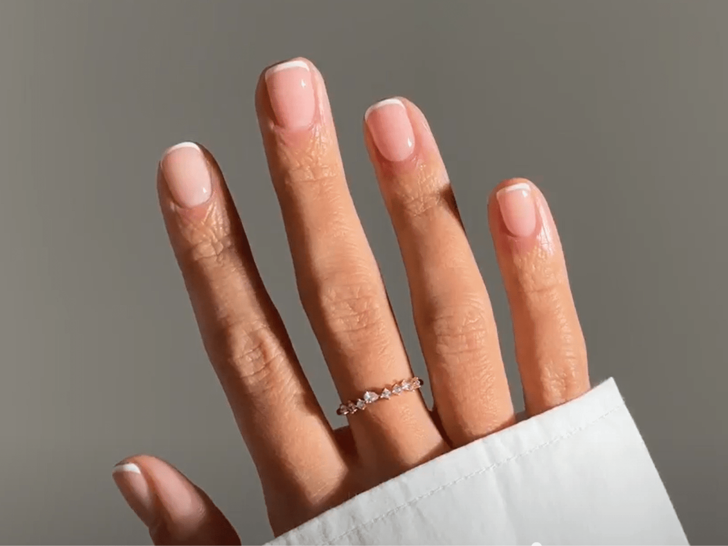 A hand with a ring on the middle finger and cared for with a French manicure.