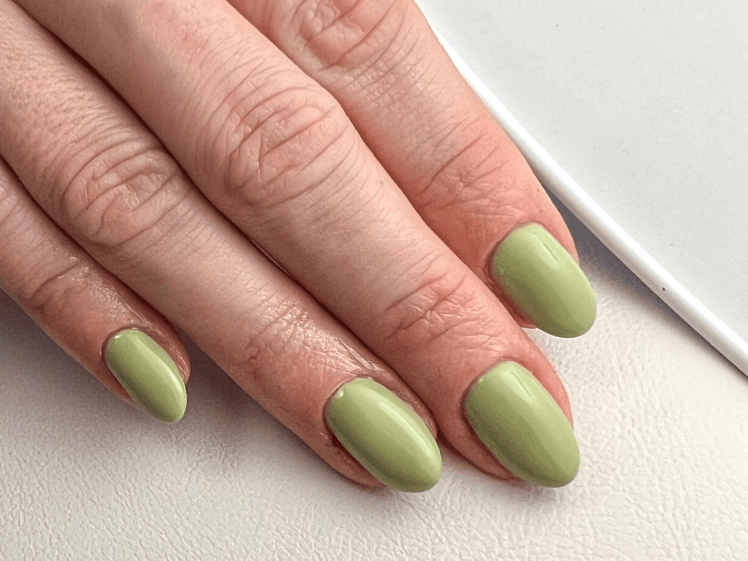 A hand with green painted nails on a white background.