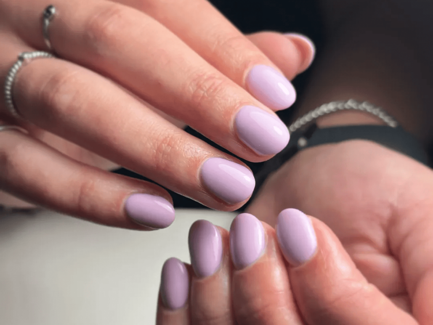 Two hands with lavender nail polish and silver rings.