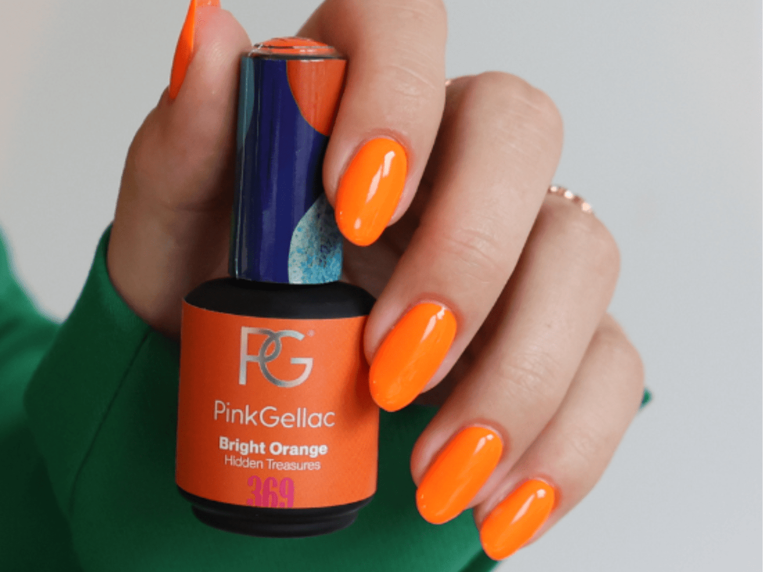 A hand with bright orange nail polish holds a bottle of Pink Gellac Bright Orange nail polish.