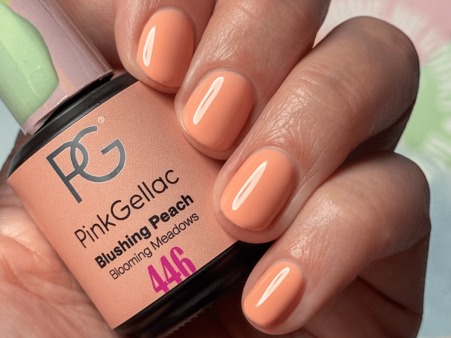 A hand with short-manicured nails painted in a peachy color, next to a bottle of Pink Gellac nail polish in the shade "Blushing Peach".