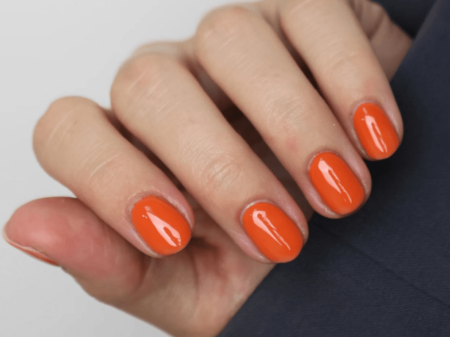 A hand with short, rounded nails painted in a striking orange color.