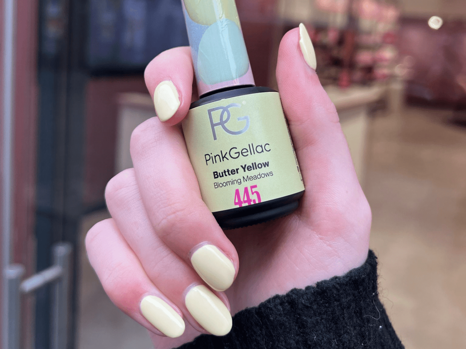Hand with pastel yellow nails holds a bottle of Pink Gellac