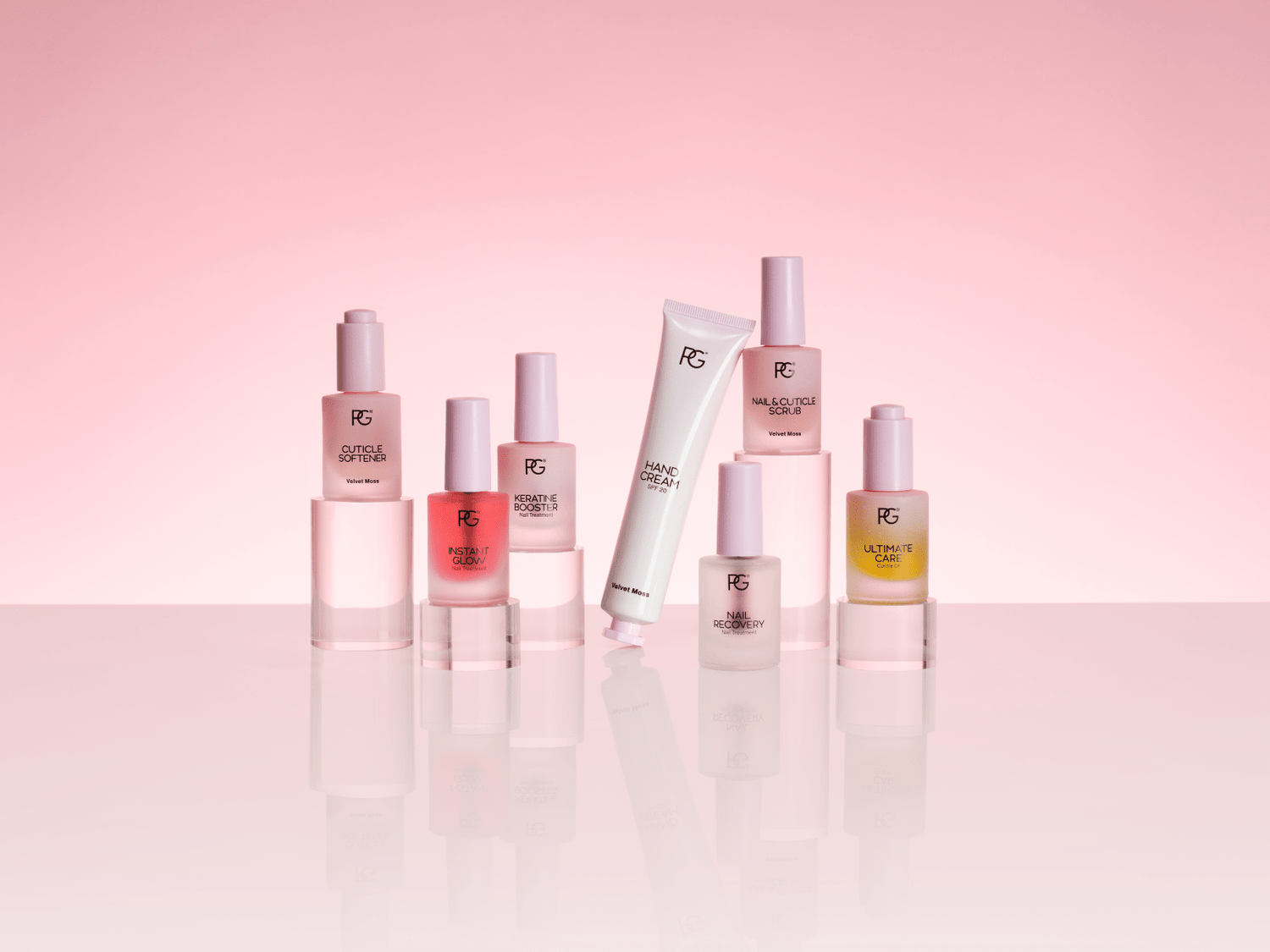 Several bottles of cosmetics and a tube of hand cream on a mirrored surface with a pink background.