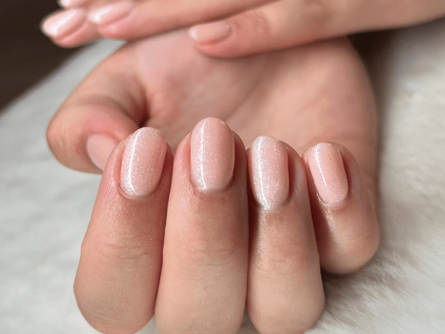 Hand with short, shiny, light pink nails against a soft background.