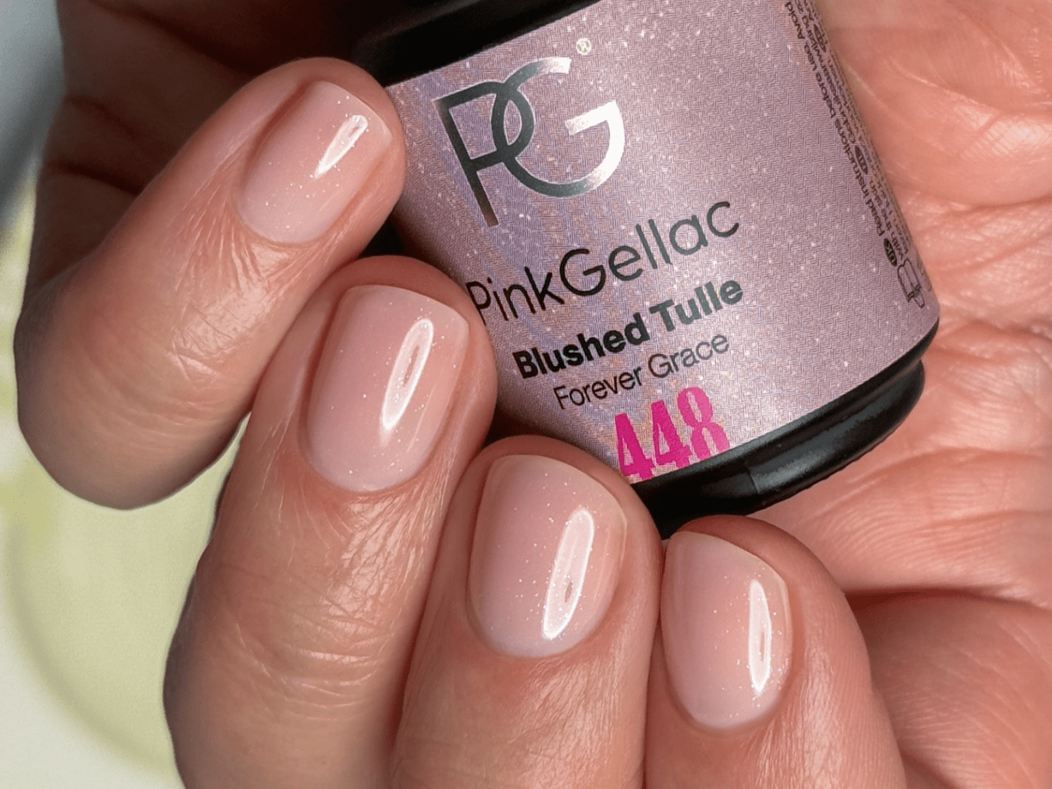 Close-up of a hand wearing light pink nail polish, holding a bottle of Pink Gellac "Blushed Tulle" (448).