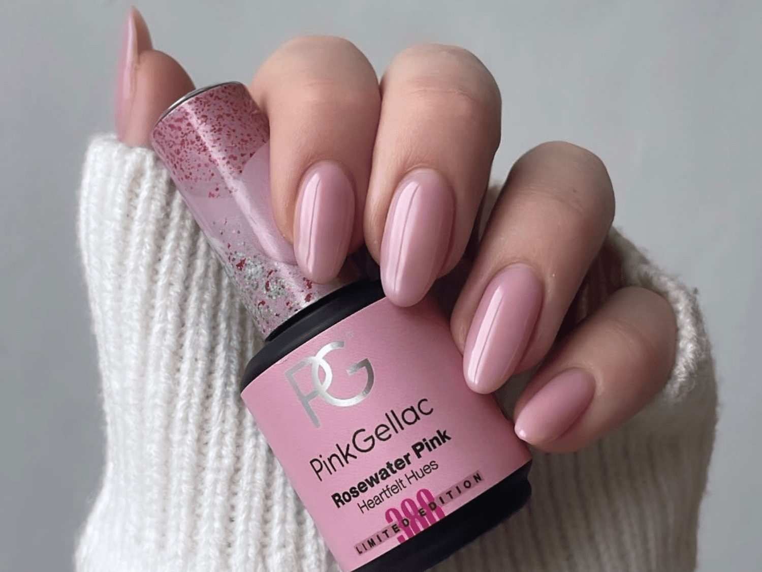 Hand with pink gel nails, holding a bottle of Pink Gellac Rosewater Pink nail polish; white background.
