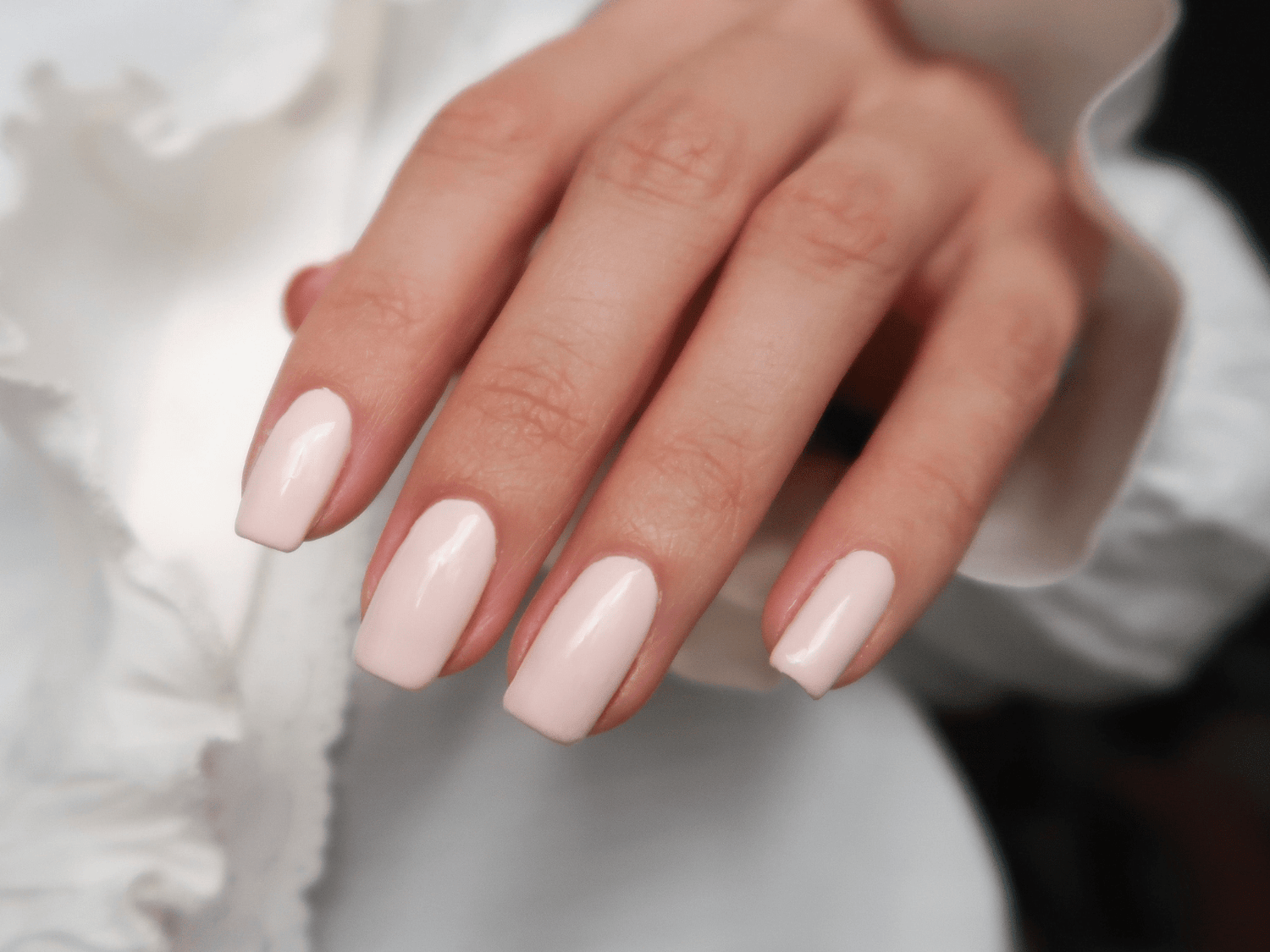 A hand with long, square nails painted in a light, shiny pink color.