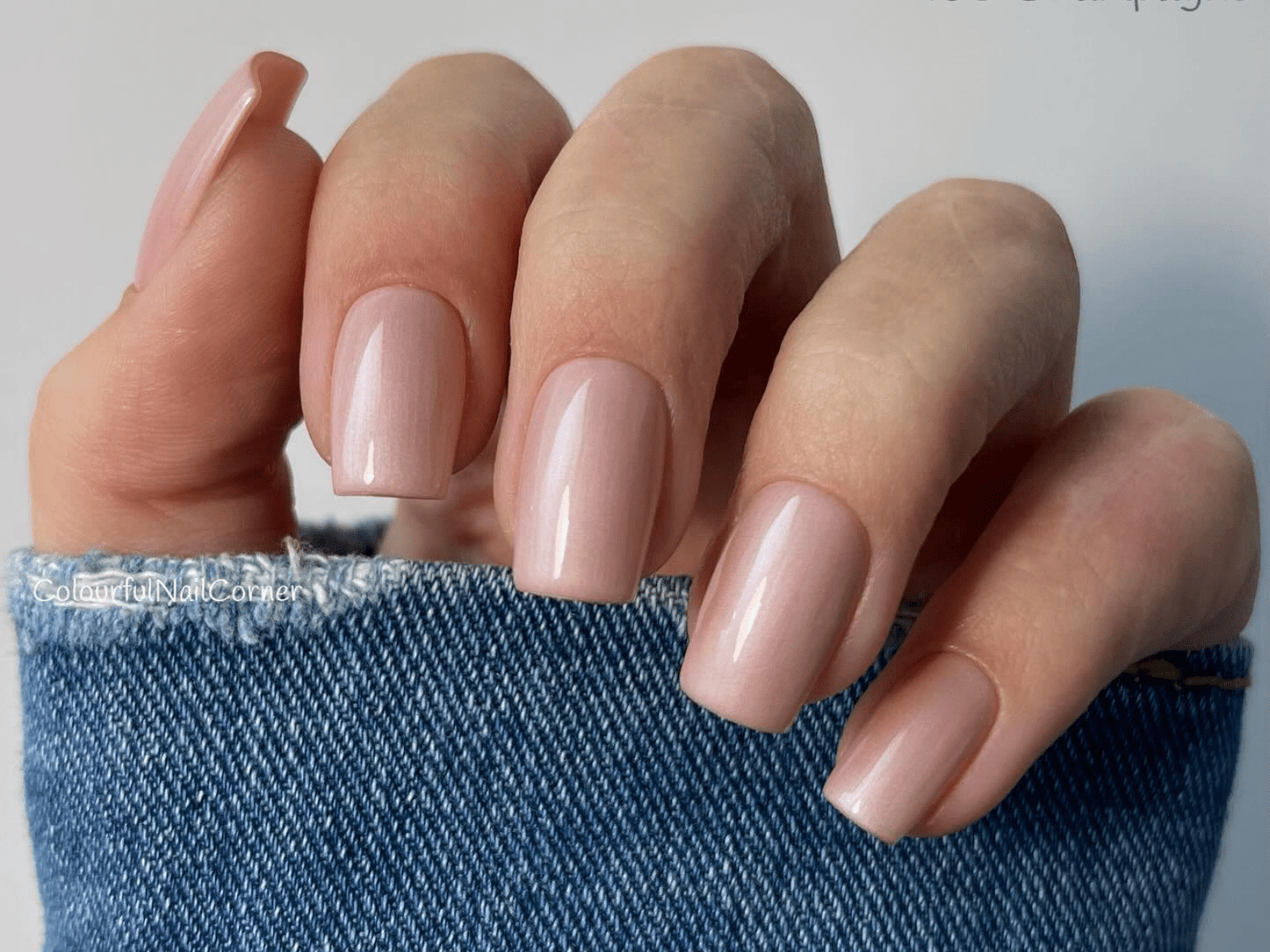 Hand with shiny nude false nails, covered with blue denim fabric.