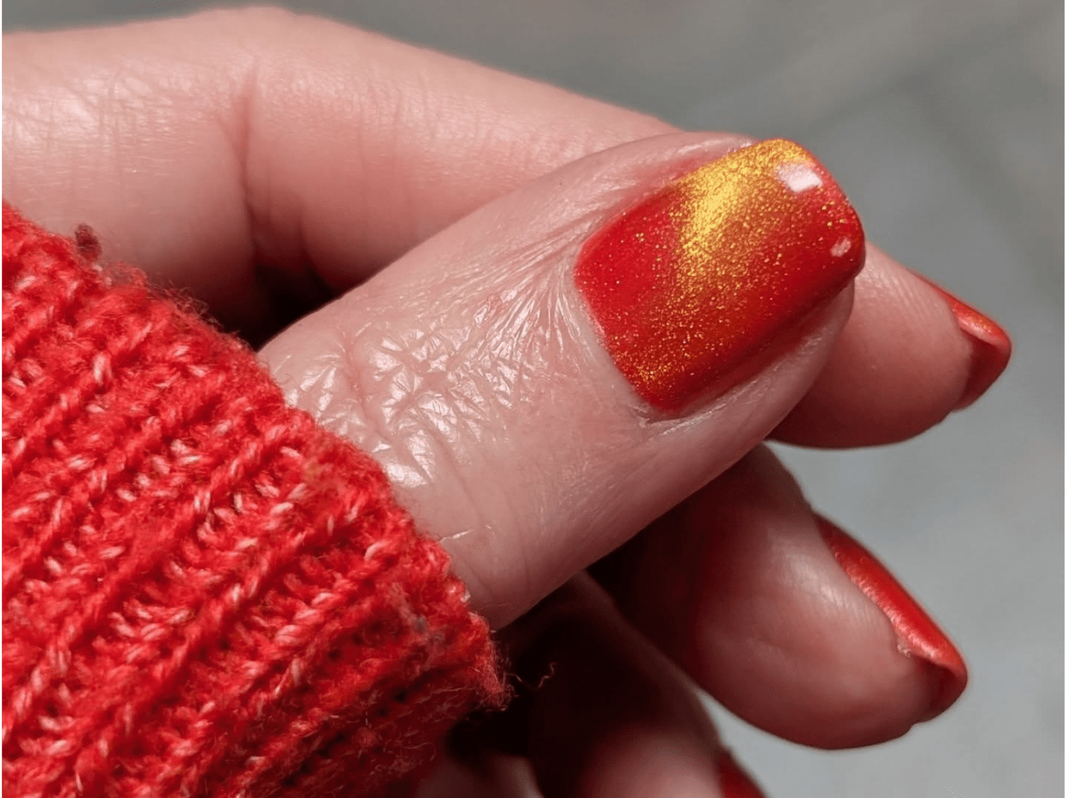 Red knitted sweater and a nail with red and yellow shiny nail polish.