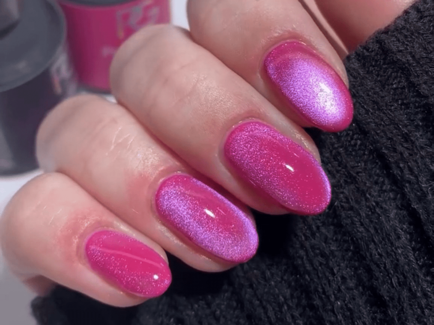 Pink nails with a pearly shine and glitter, against a dark background.