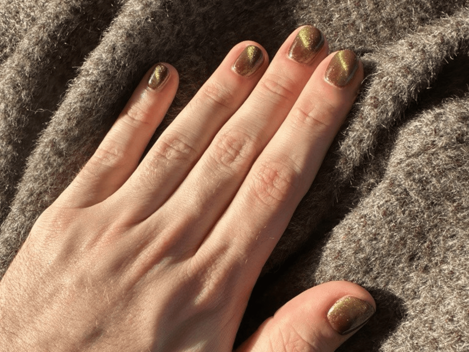 Hand with gold painted nails on a brown, woolly fabric.